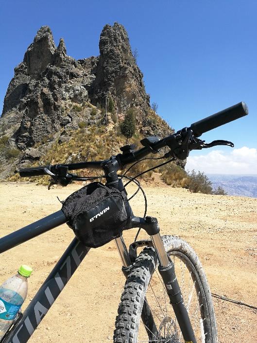 Fotografía a colores de manubrio de bicicleta en ascenso cerca de una roca al borde del camino de terracería.