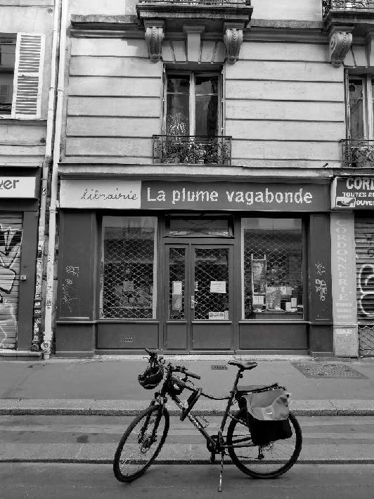 Fotografía en blanco y negro de una bicicleta estacionada en la calle frente a fachada de librería frances La plume vagabonde